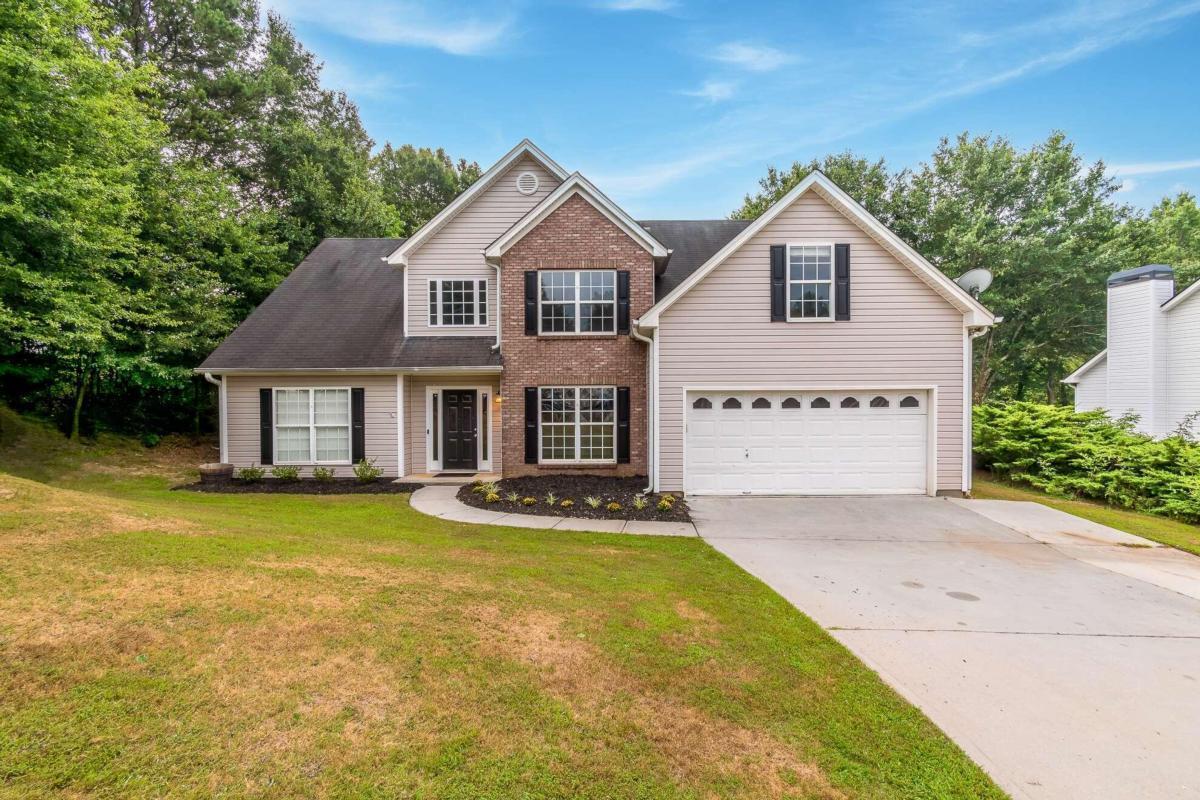 Two-story brick-and-siding house with an attached garage, concrete driveway, and mature trees.