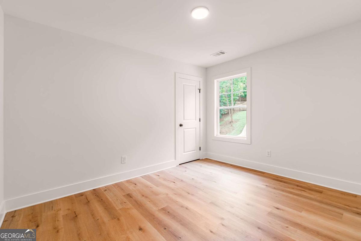 Empty room with hardwood floors, gray walls, and a window overlooking greenery.