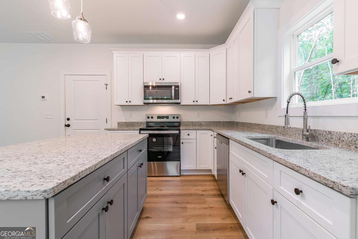 Bright kitchen with gray island, white cabinetry, granite counters, and stainless steel appliances.