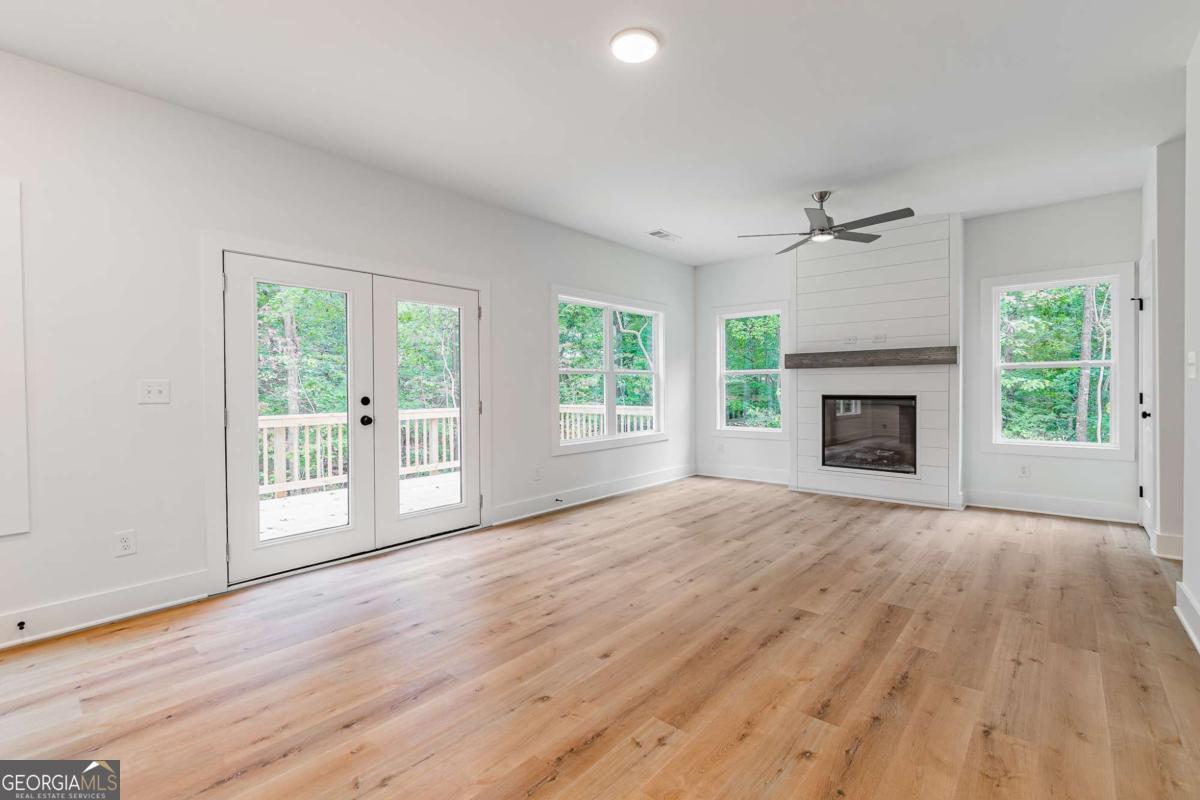 Vacant living room with a shiplap fireplace, light wood floors, and French doors opening to a wooded deck.