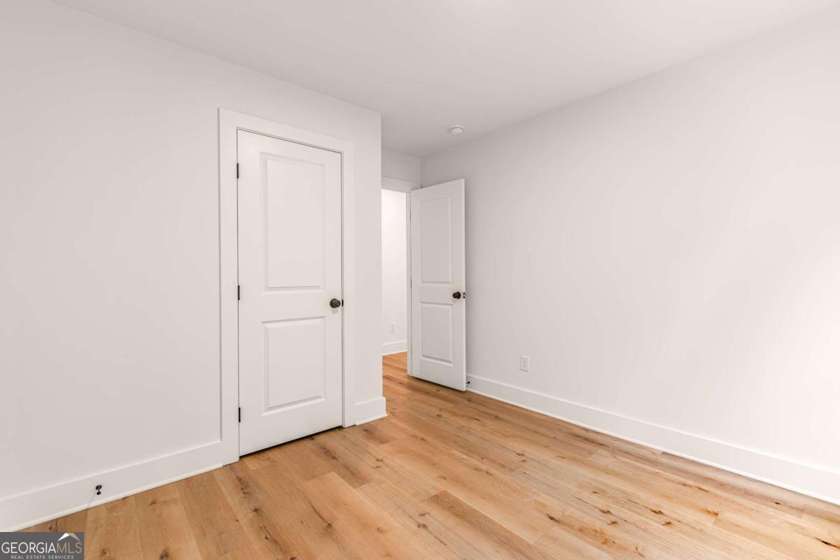 Empty room with light wood flooring, white walls, and two paneled doors.