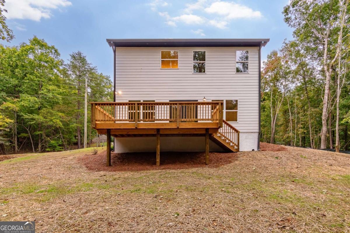 Rear of a two-story home with a raised wooden deck overlooking a wooded yard.