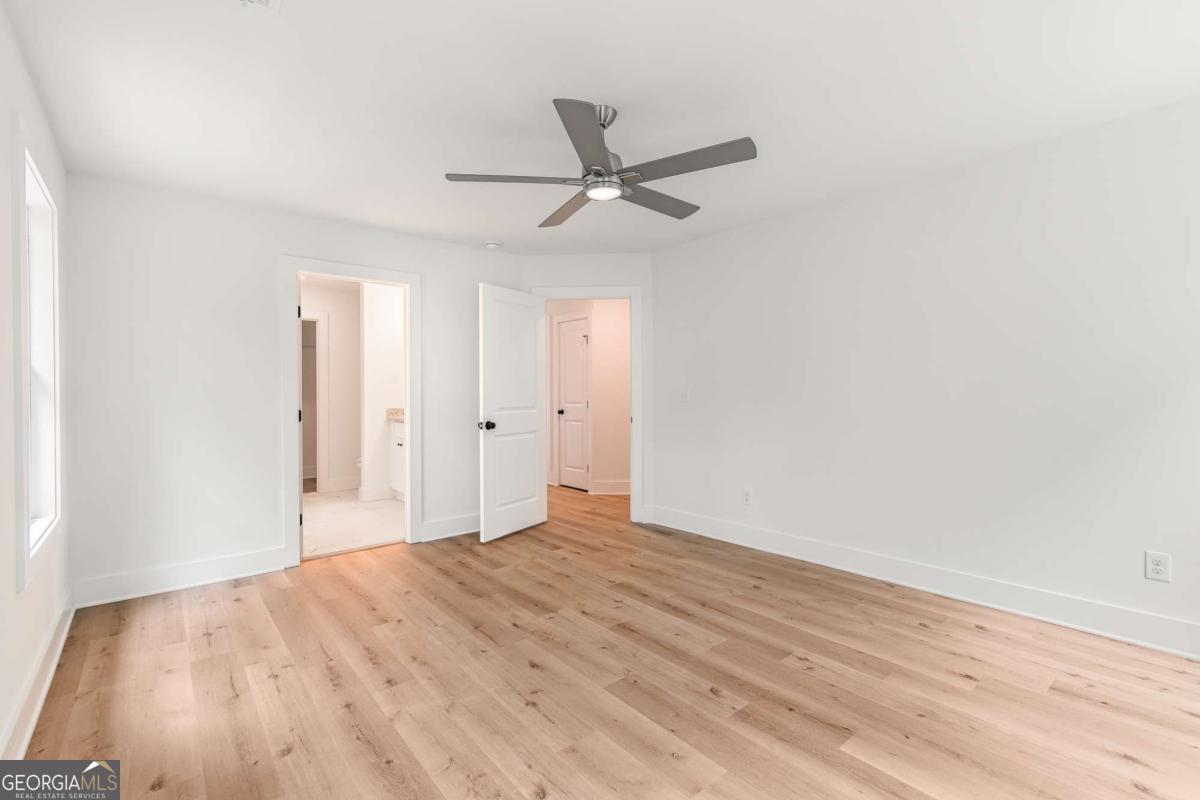 Empty bedroom with light wood floors, a ceiling fan, and two open doorways.