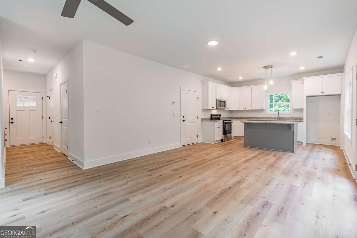 Open kitchen and entry with white cabinets, gray island, and light wood floors.