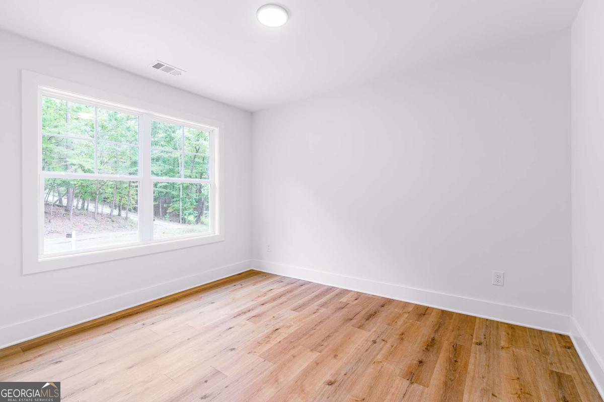 Empty bedroom with light wood flooring and a large window overlooking trees.