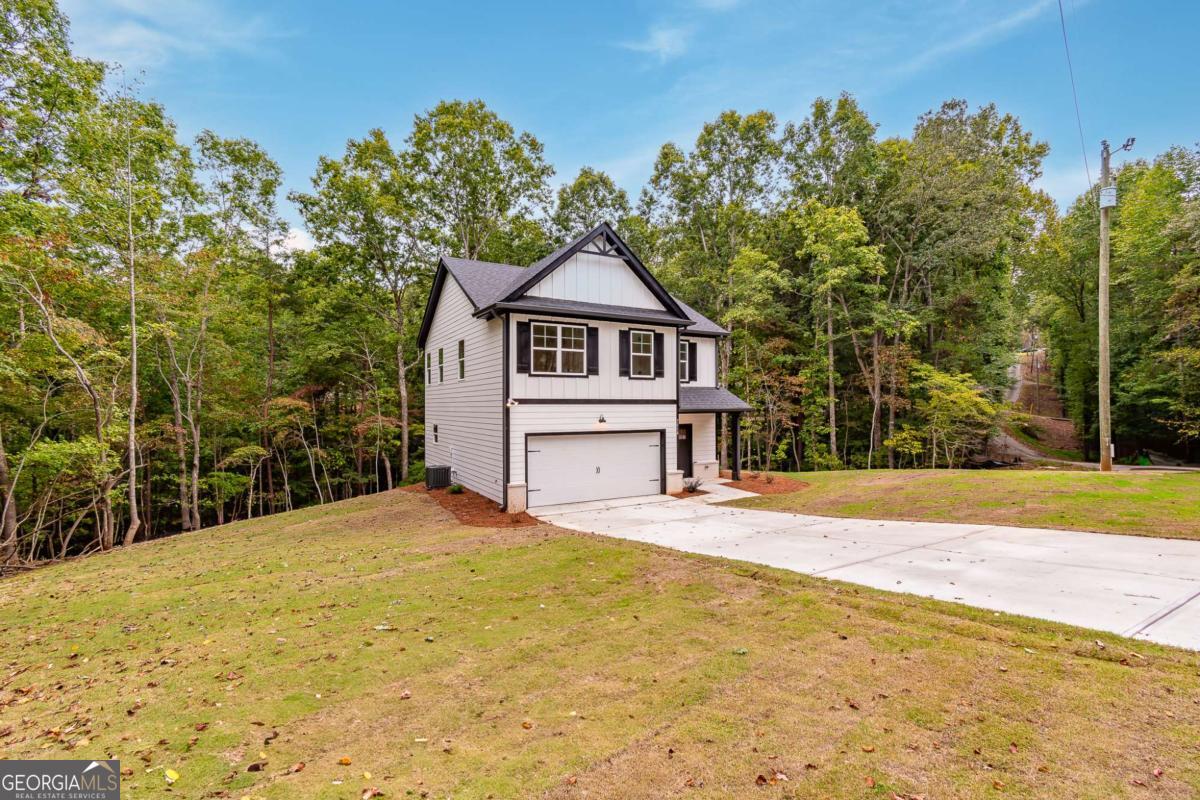 Two-story white house with dark trim, a double garage, and a wooded setting.