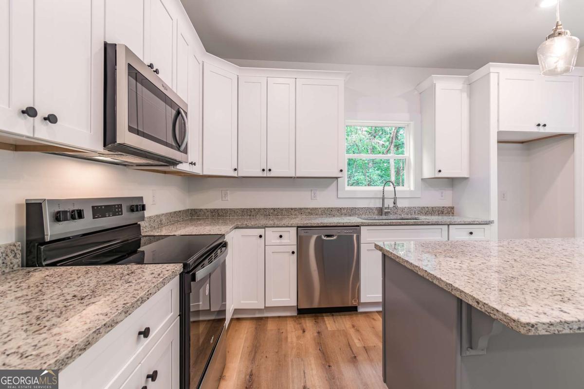 Kitchen with white cabinets, granite counters, stainless steel appliances, and a large island.