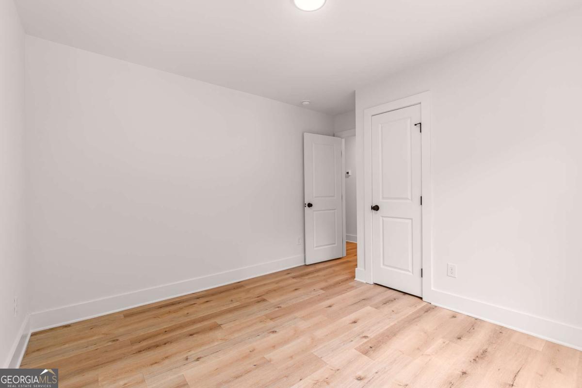 Empty room with light wood floors, white walls, and two paneled doors.