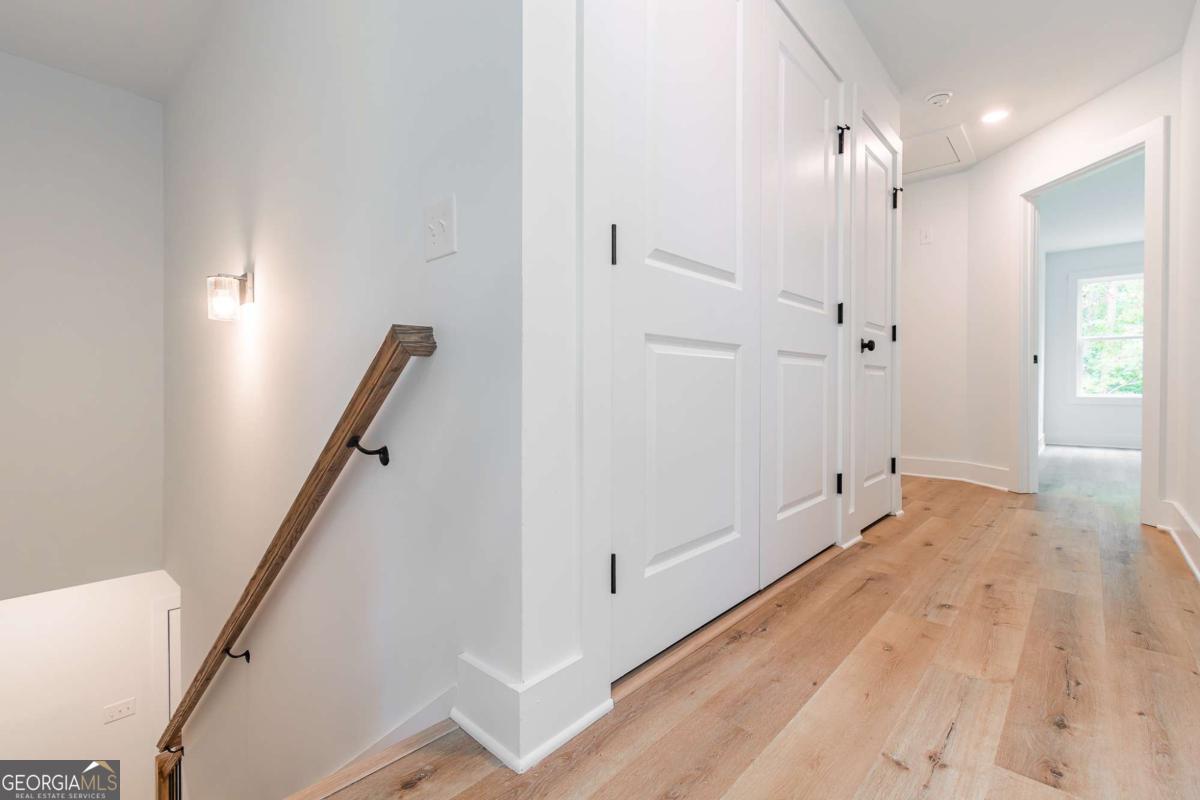 Bright hallway with light wood floors, white paneled doors, and a wood stair handrail.