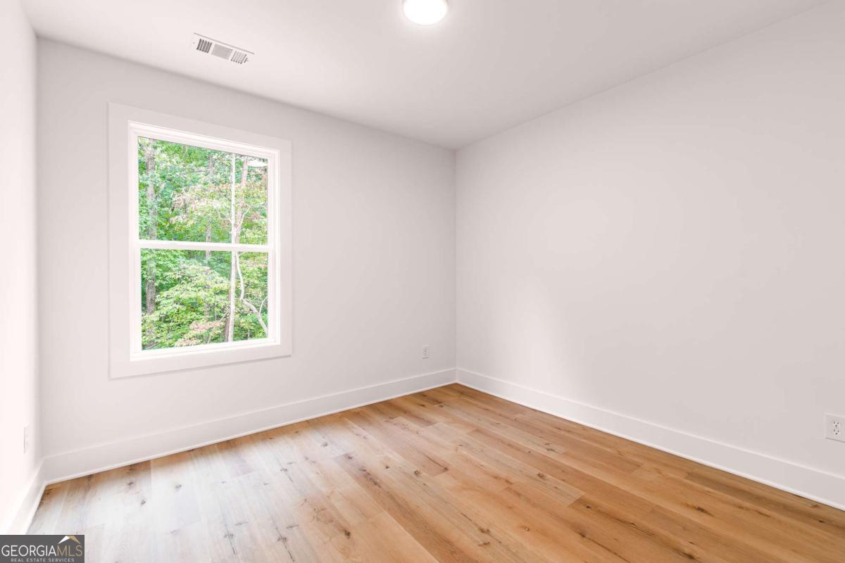 Empty room with light wood floors and a large window overlooking trees.