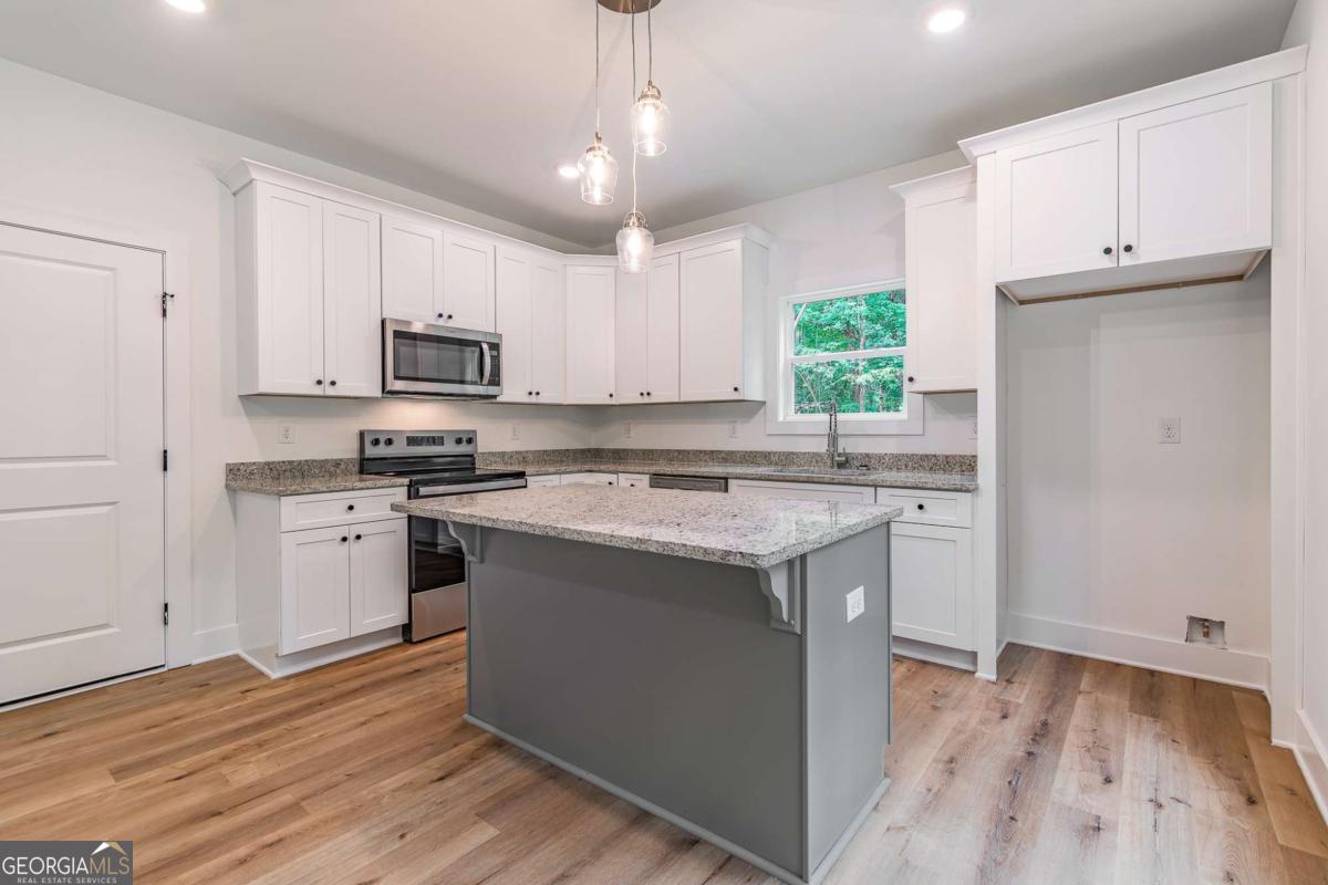 Kitchen with white cabinets, stainless appliances, a granite-topped island, and a window overlooking trees.