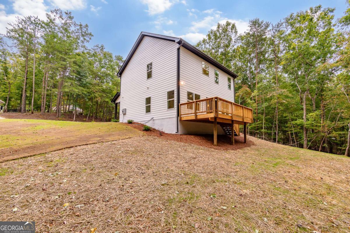 Two-story house with a raised wooden deck on a sloping, wooded lot.
