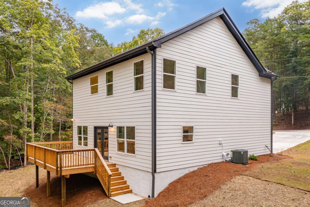 Two-story white-sided house with a raised wooden deck and stairs, surrounded by trees.