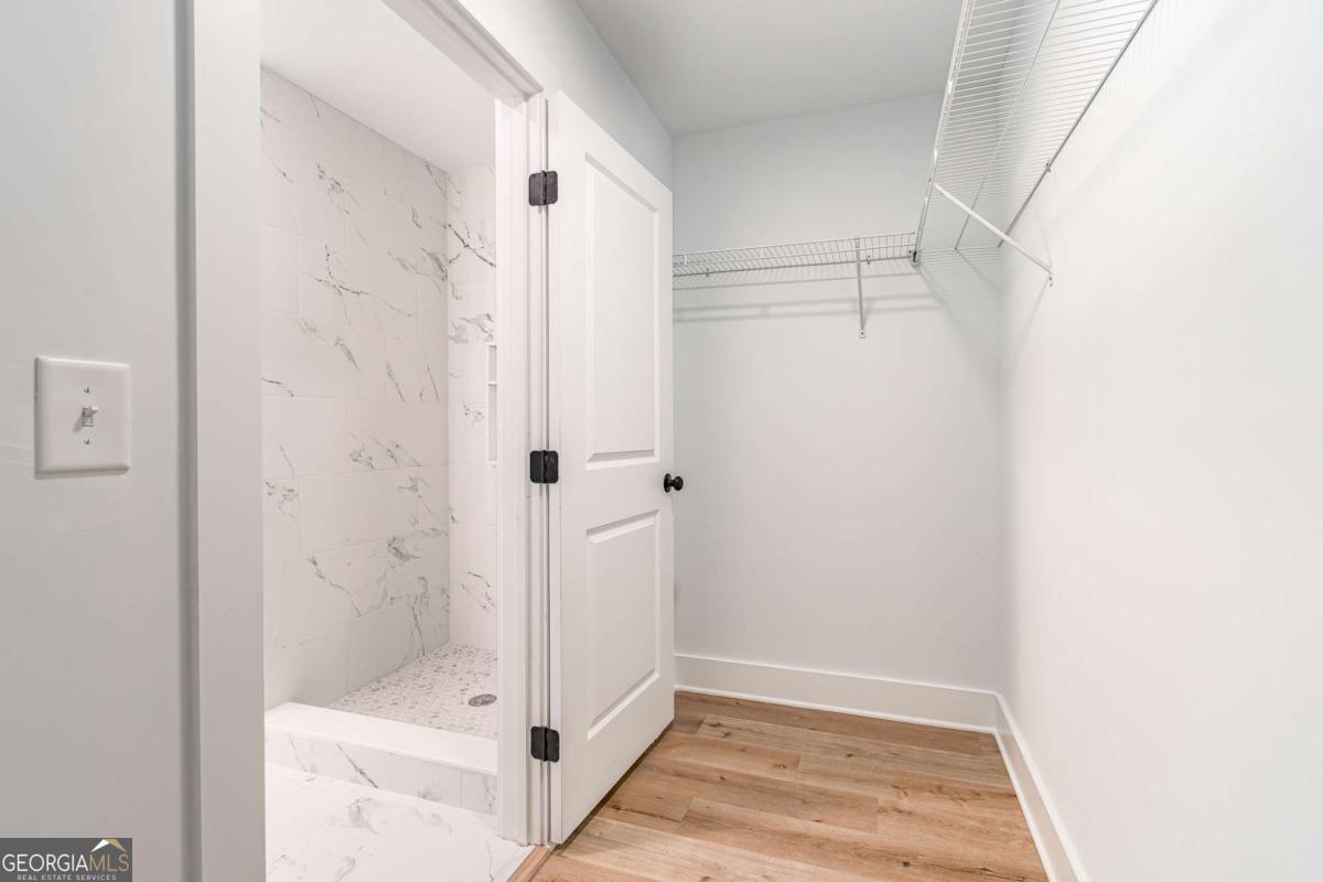 Walk-in closet with white wire shelving beside a marble-look tiled shower.