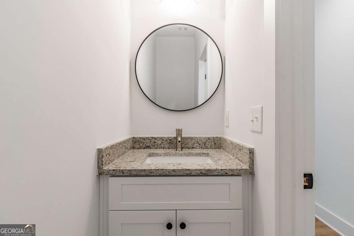 Powder room vanity with speckled granite counter, white cabinets, and round mirror.