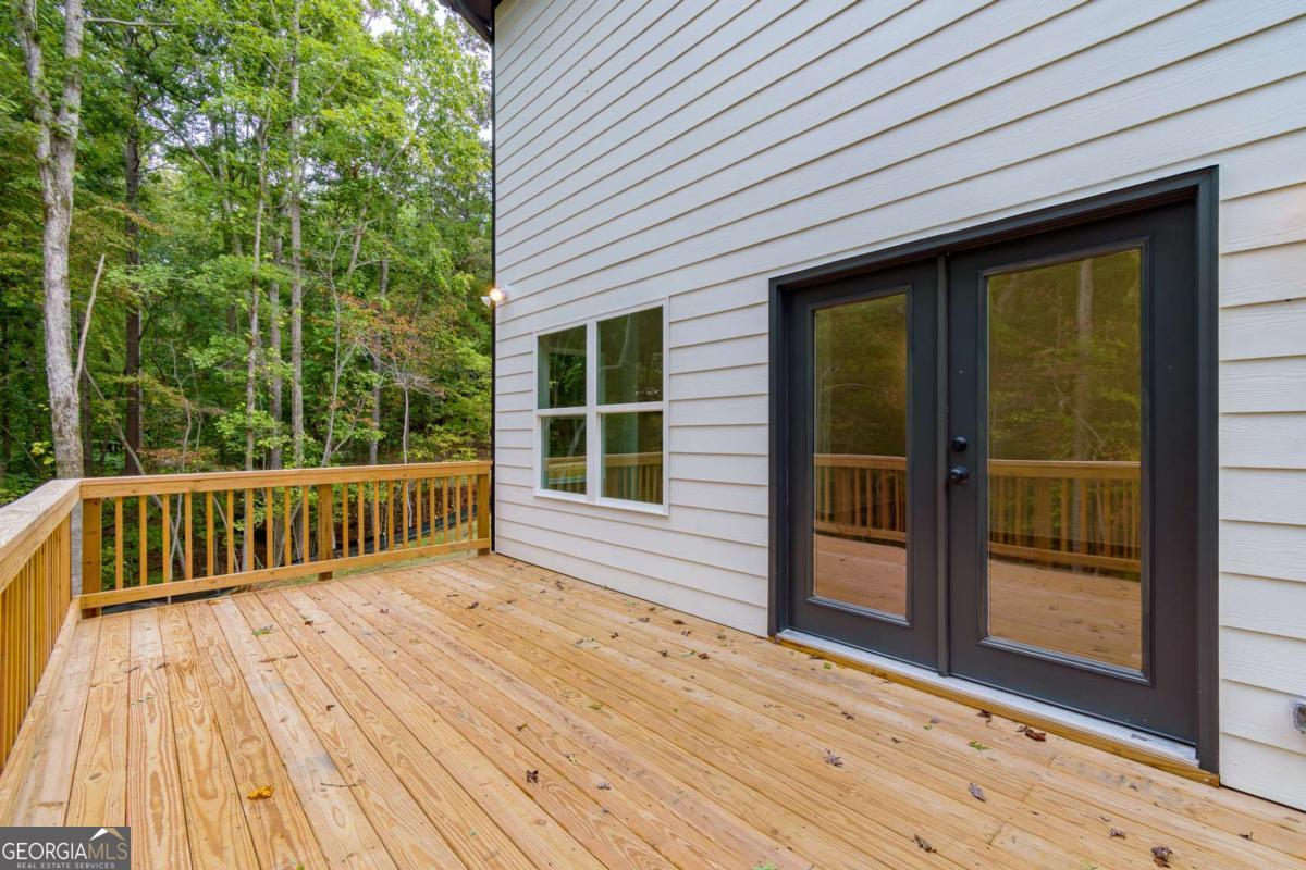 Wood deck beside a light-sided house, with black-framed glass doors and a wooded backdrop.