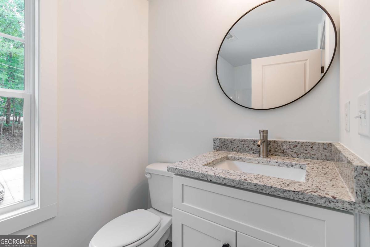 Bright bathroom with a granite-topped white vanity, round mirror, toilet, and tall window.