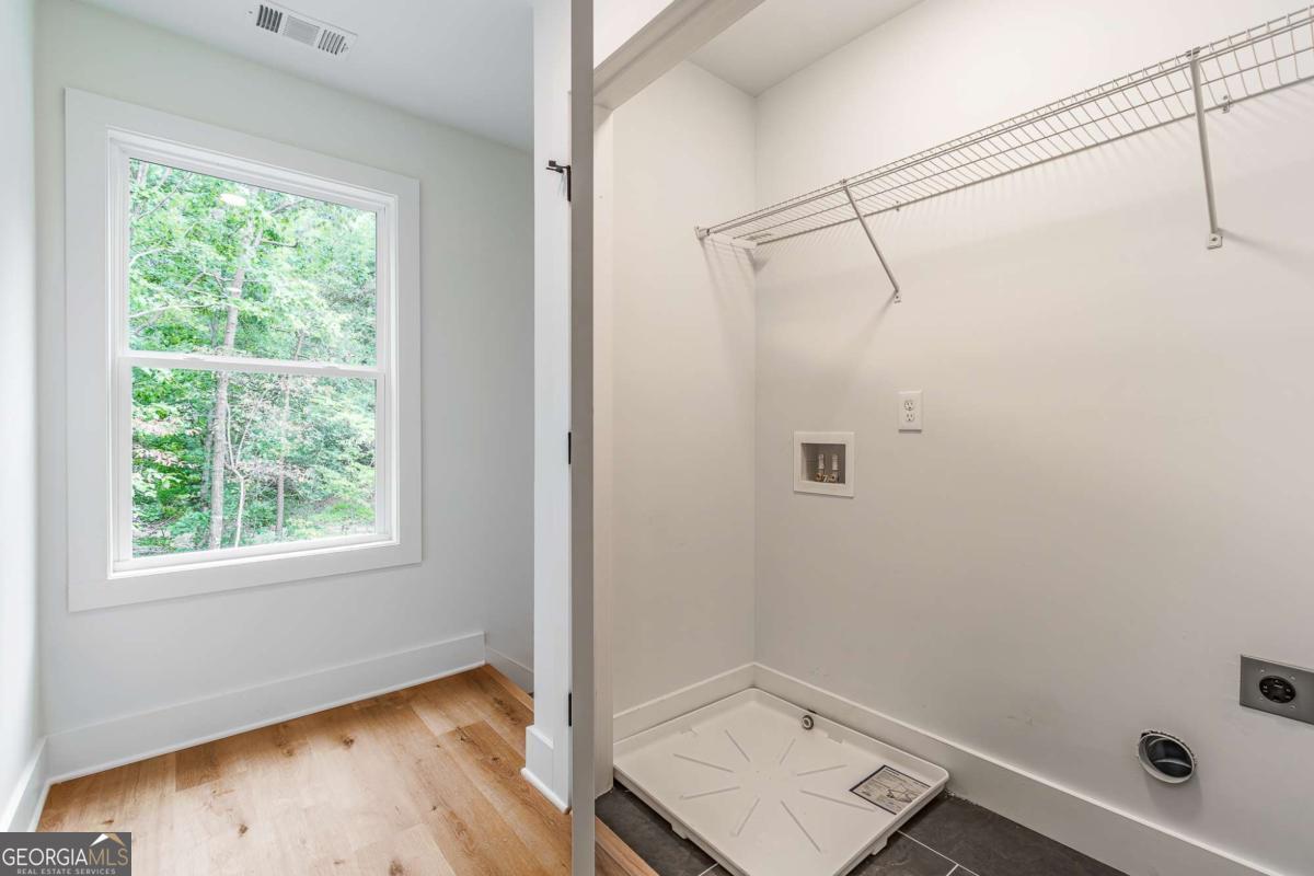 Laundry area with washer-dryer hookups and a wire shelf beside a window overlooking trees.