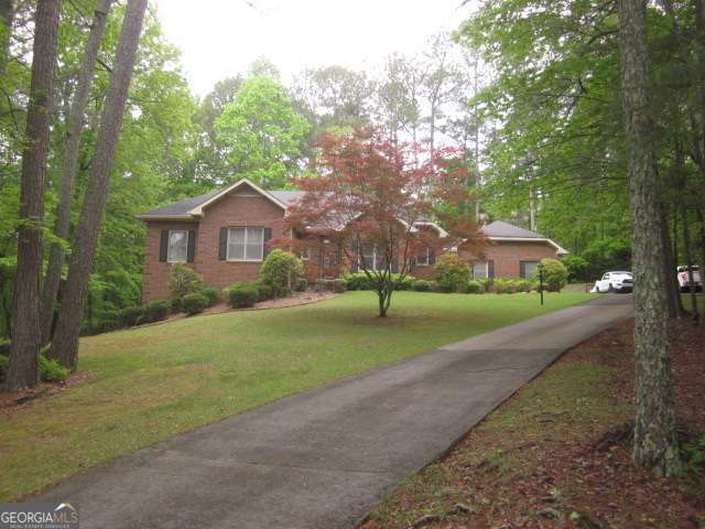 Brick home among mature trees, with a landscaped lawn and paved driveway.