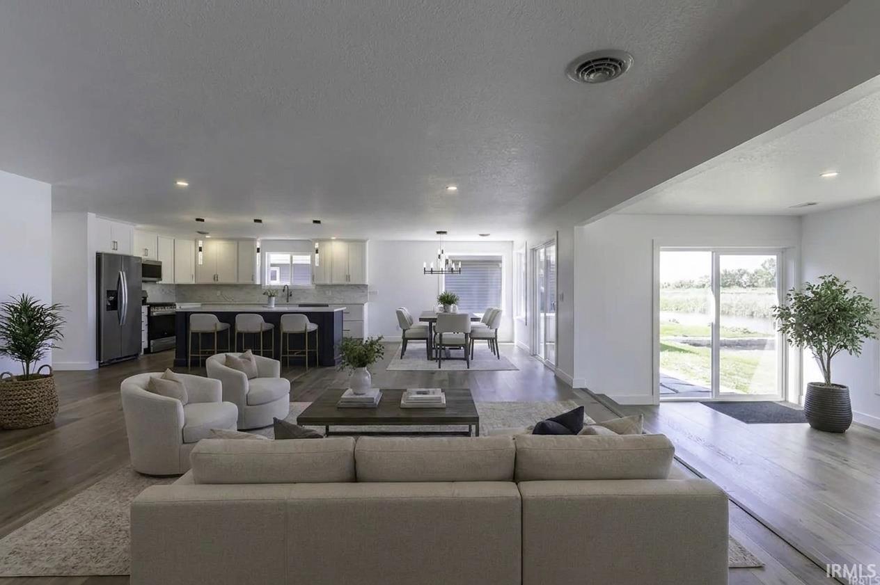 Open-plan living room with a large sectional, white kitchen, dining area, and sliding doors overlooking water.