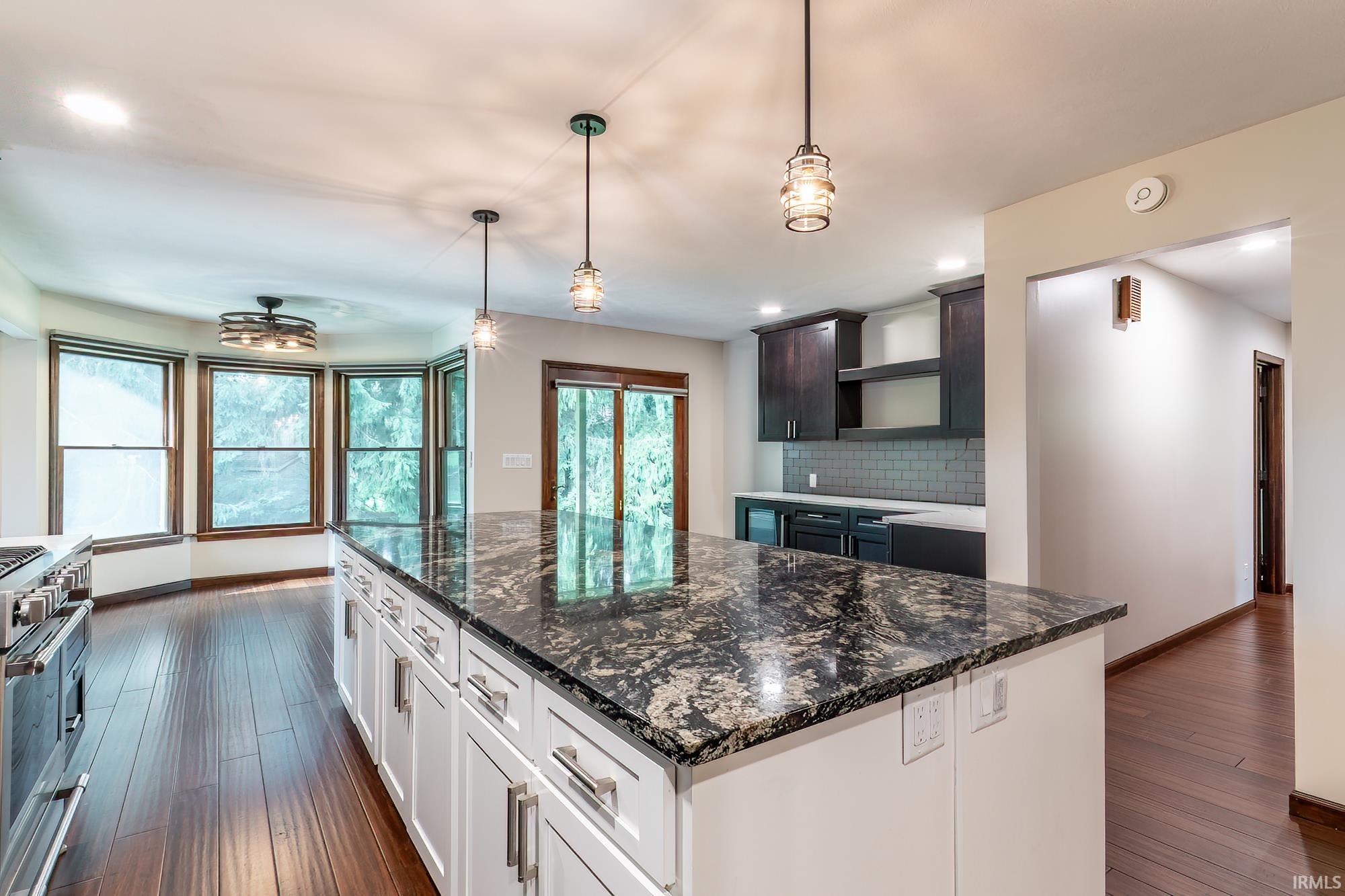 Kitchen with a large dark granite island, dark cabinetry, stainless range, and wood-trimmed windows.