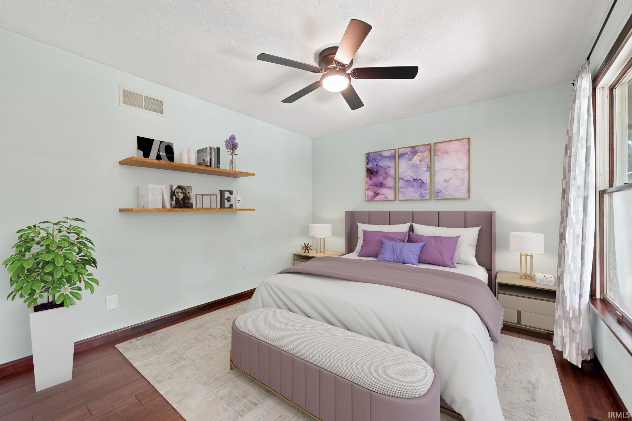 Staged bedroom with a mauve bed, purple pillows, floating shelves, and a large curtained window.