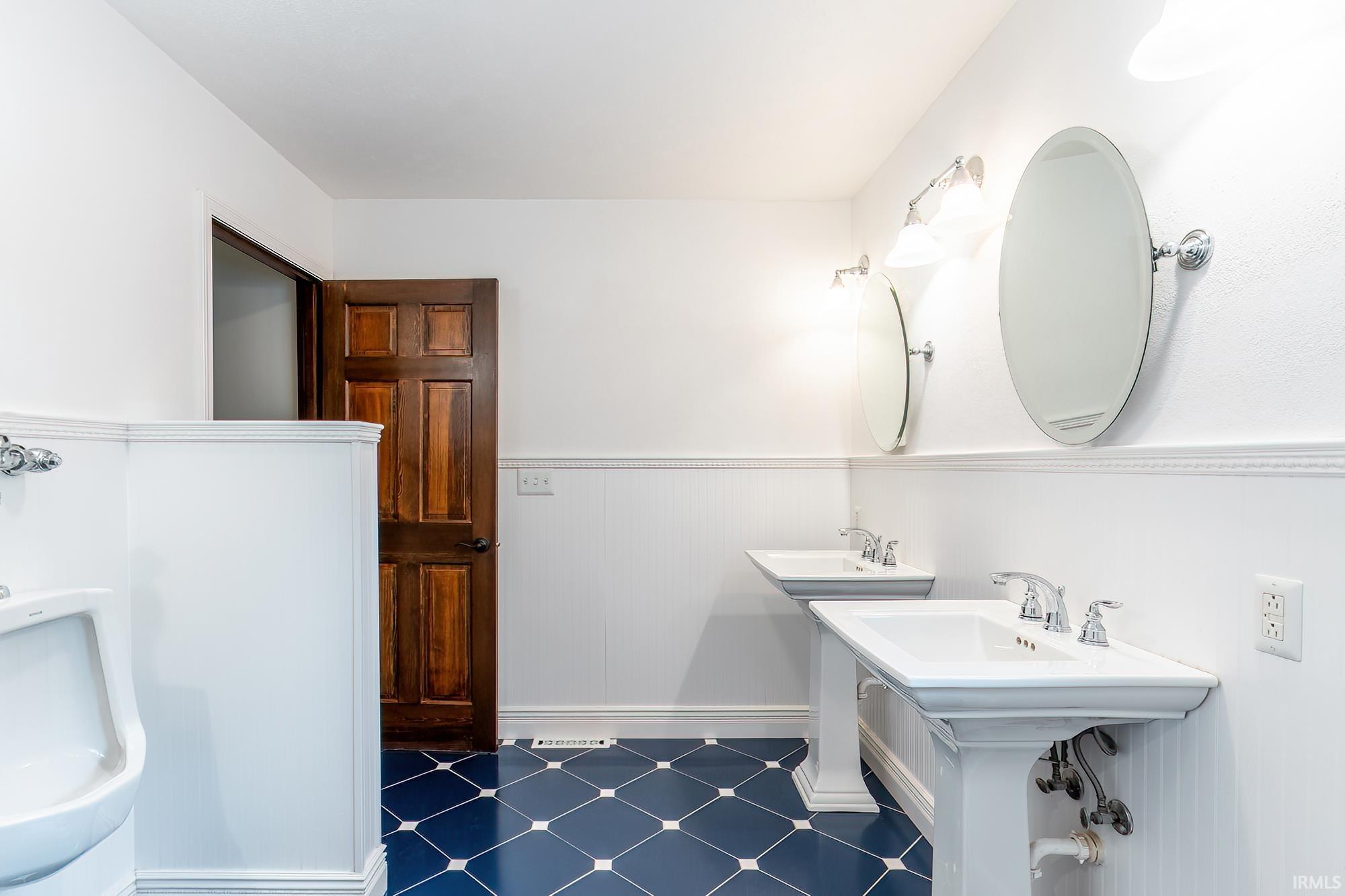 Bathroom with double pedestal sinks, oval mirrors, and blue geometric floor tile.