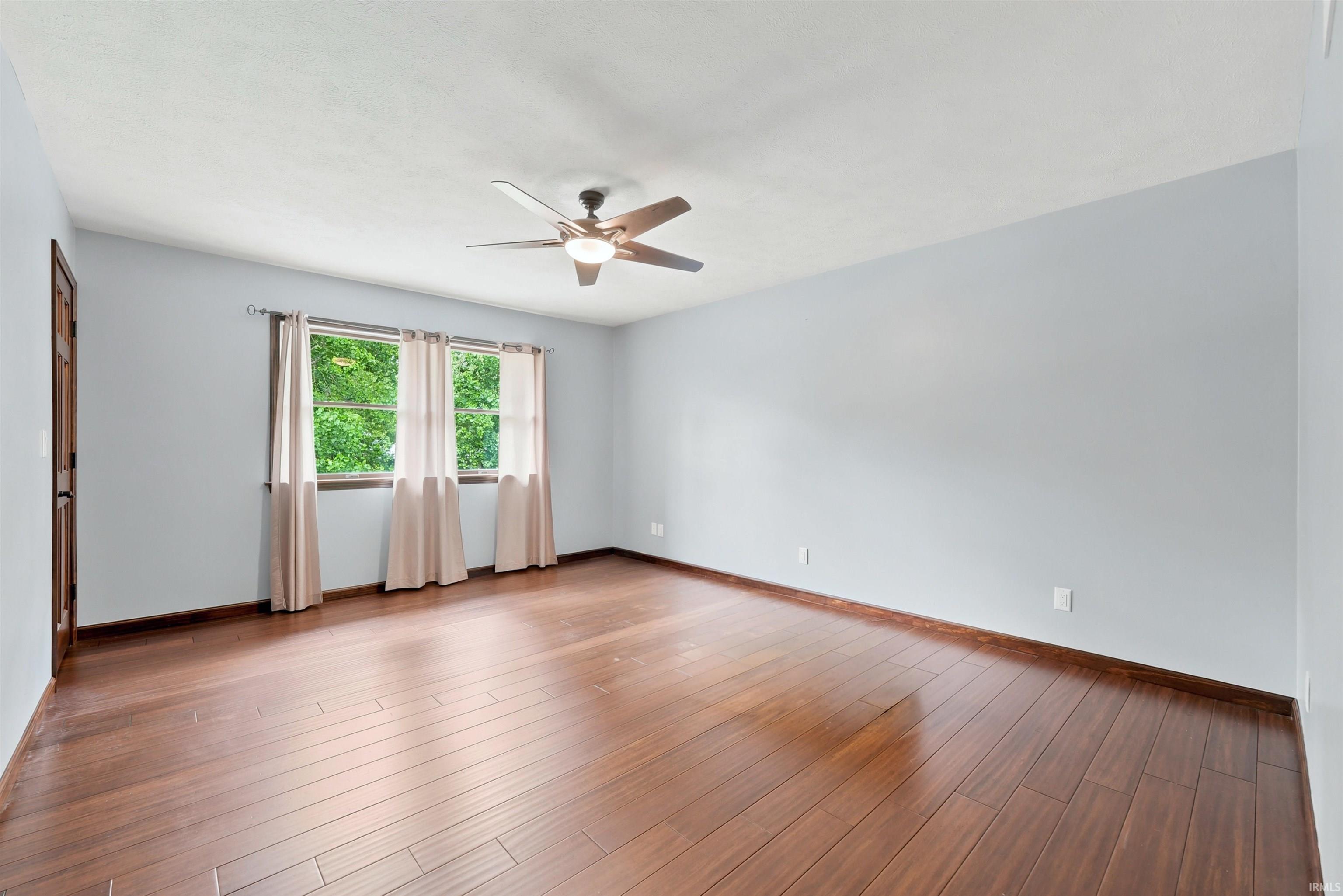 Vacant bedroom with dark wood flooring, a ceiling fan, and a curtained window.