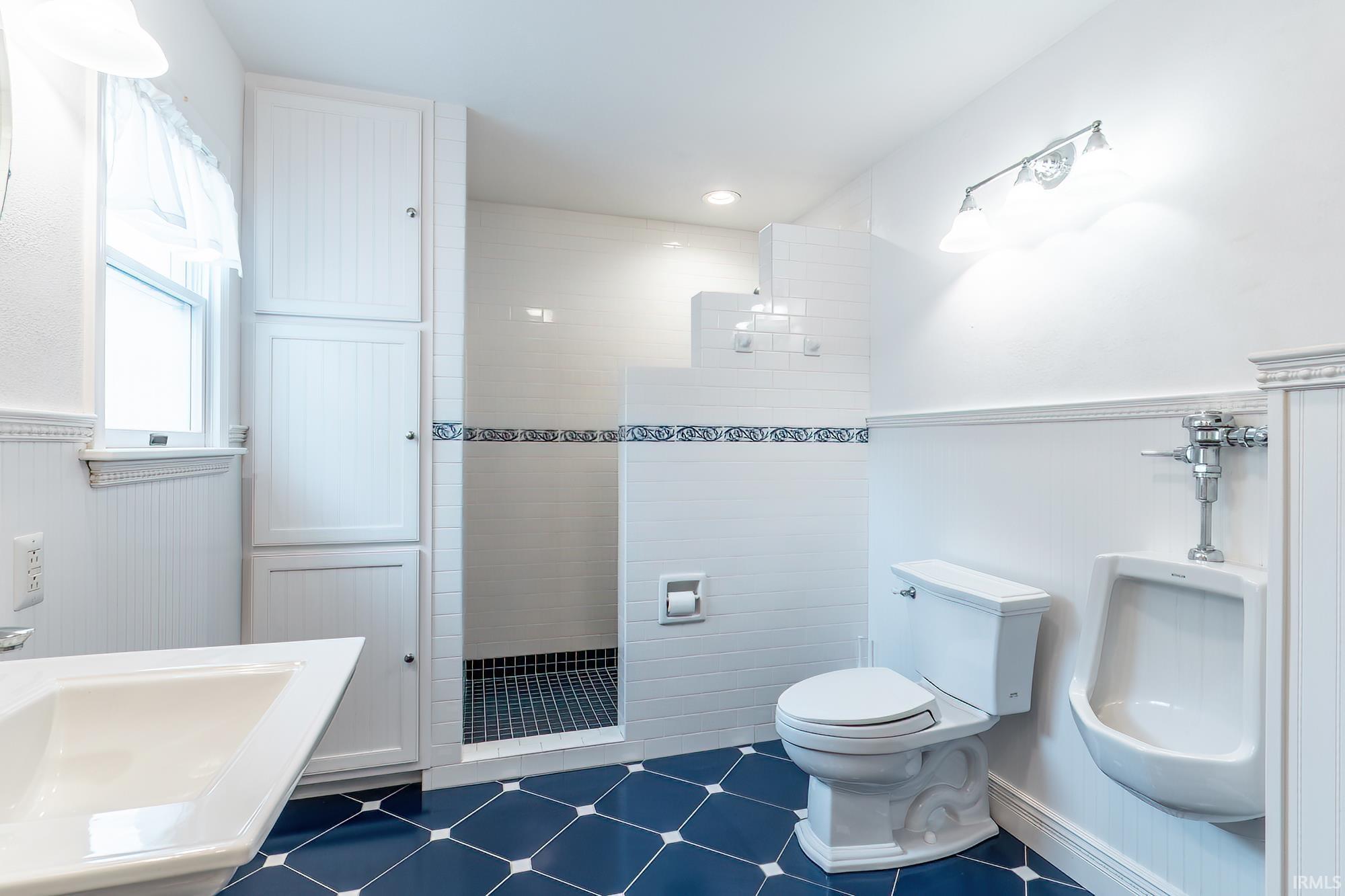 Bathroom with a tiled walk-in shower, toilet, urinal, and dark blue hexagonal floor tiles.
