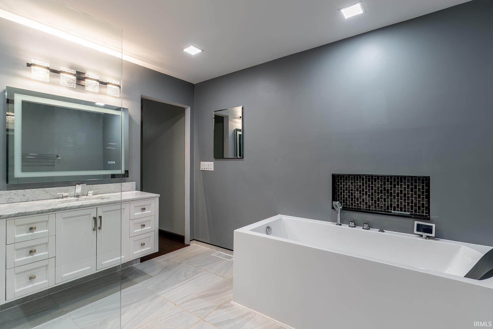 Modern bathroom with a large soaking tub, marble-topped vanity, and glass shower enclosure.