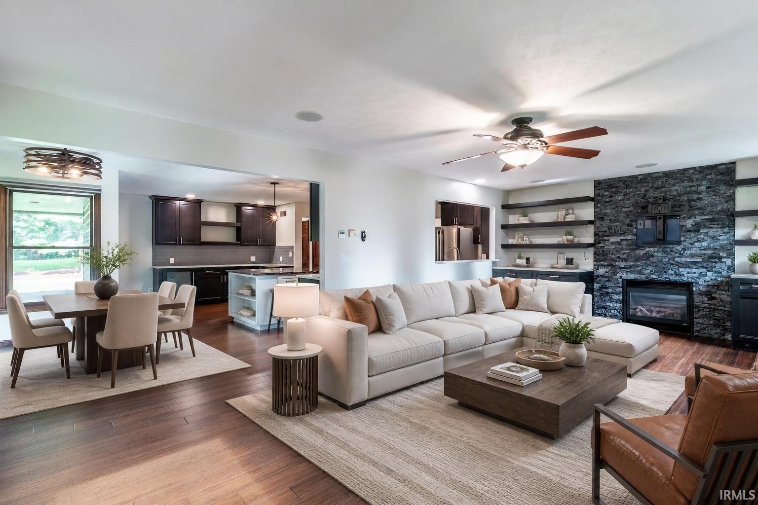 Open living and dining area with a cream sectional, dark kitchen cabinets, and a stone fireplace wall.