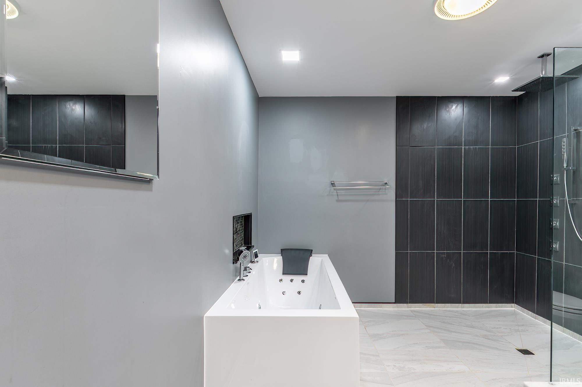 Modern bathroom with a jetted soaking tub and glass-enclosed shower with dark tile.