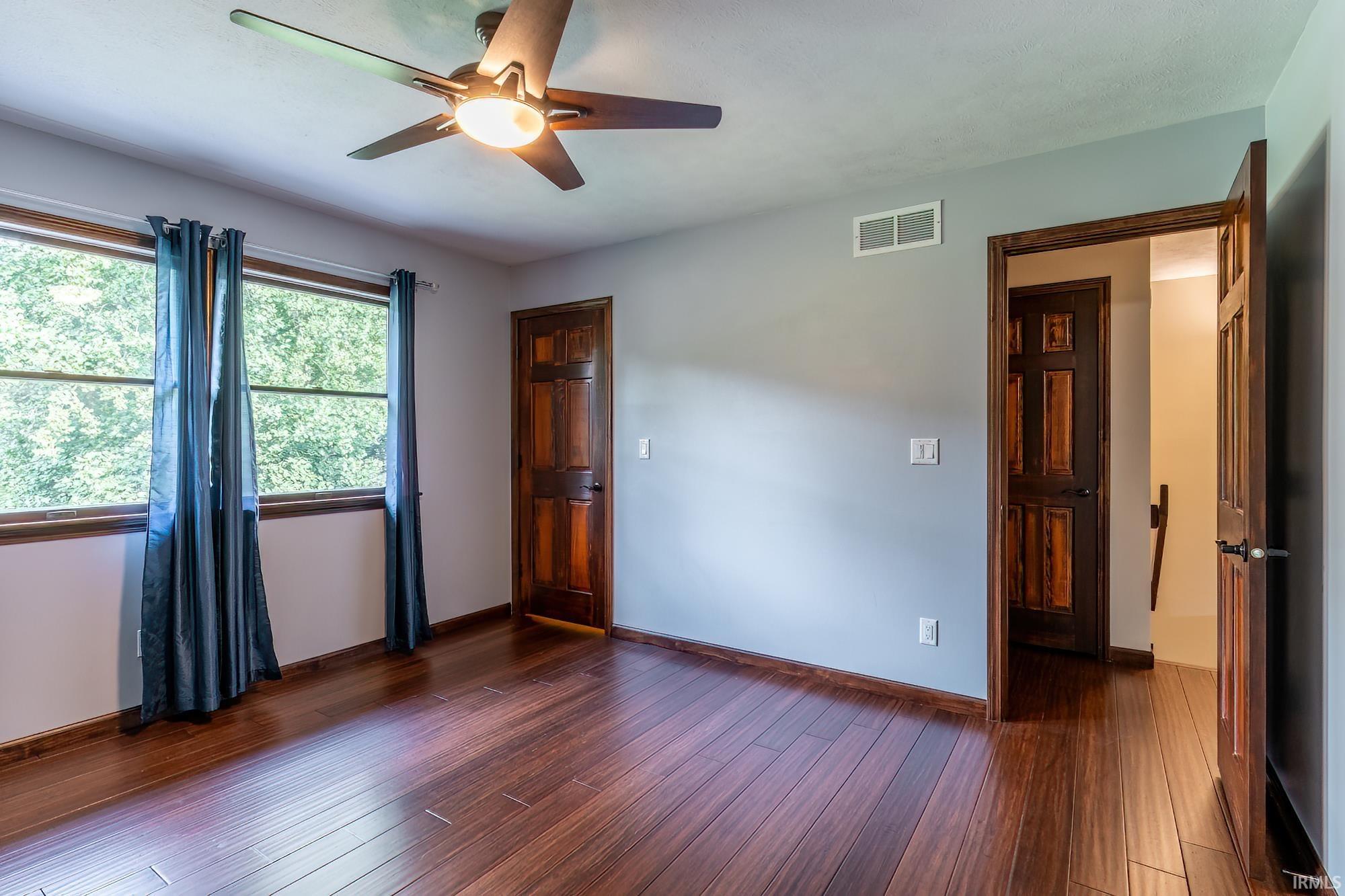 Unfurnished room with dark hardwood floors, a ceiling fan, and a large curtained window.