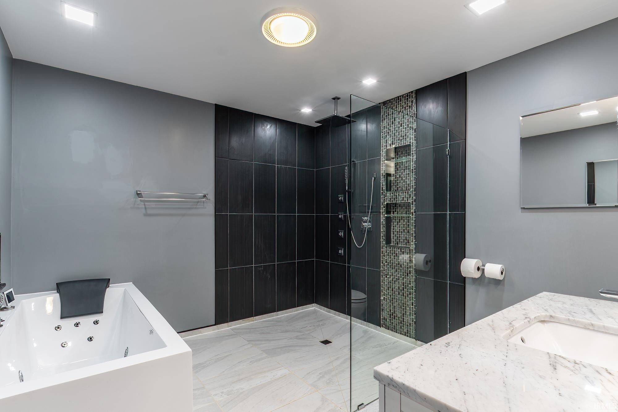 Modern bathroom with a dark-tiled glass shower, mosaic accent, soaking tub, and marble vanity.