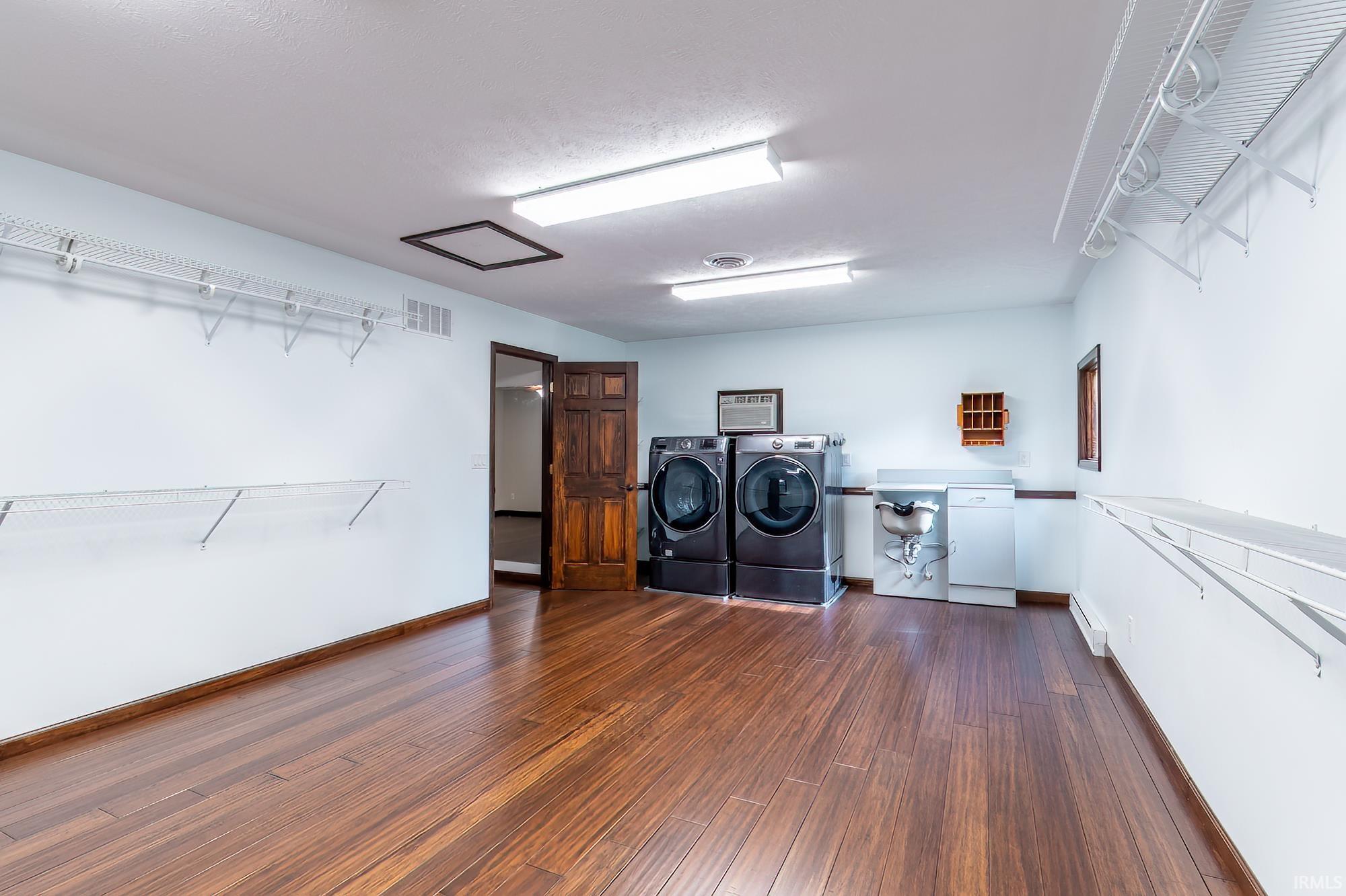 Laundry room with front-loading washer and dryer, utility sink, and wall-mounted drying racks.