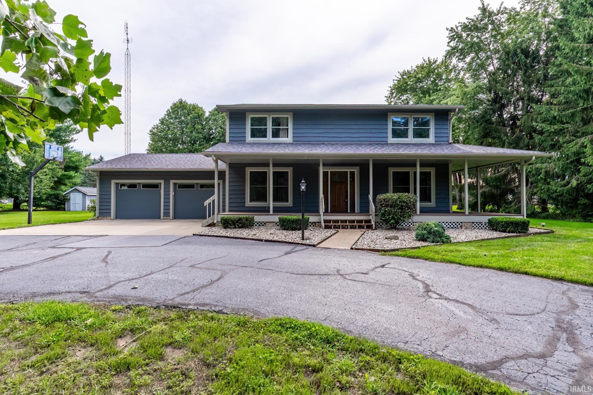 Blue two-story house with a wide covered porch, attached garage, and basketball hoop by the driveway.