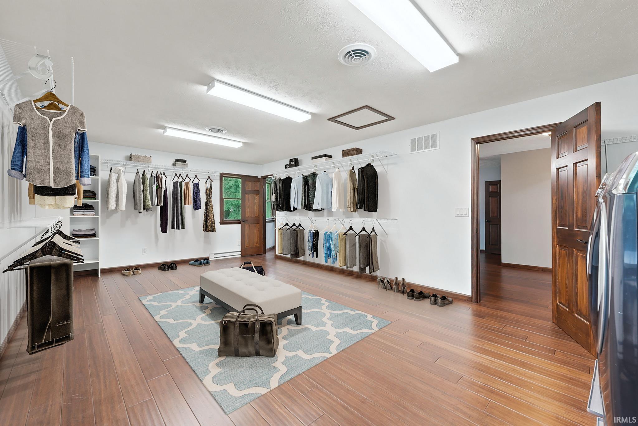 Furnished walk-in closet with open clothing racks, a central bench, and warm wood-look flooring.
