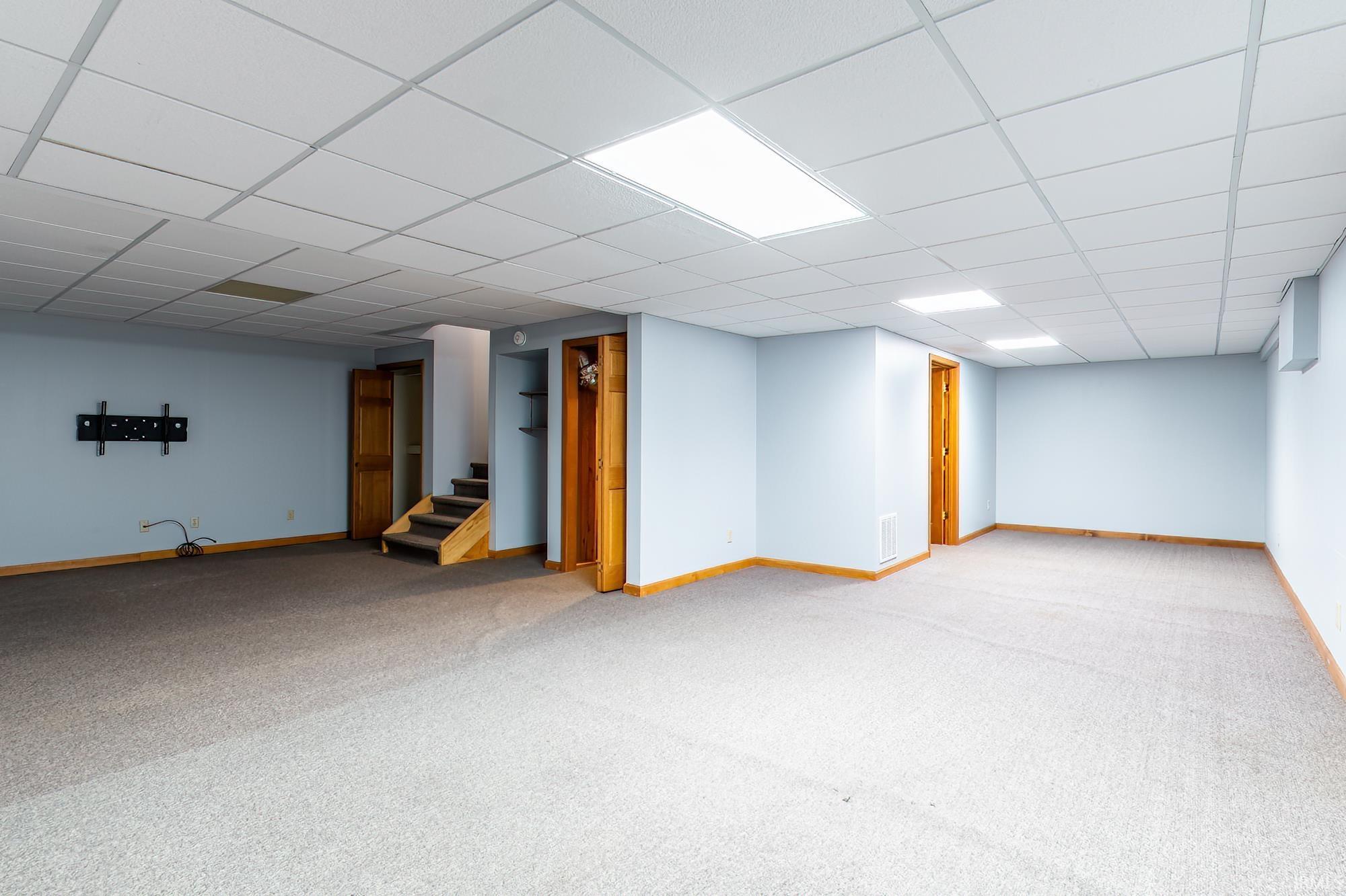 Finished basement room with gray carpet, light blue walls, and wooden stairs.