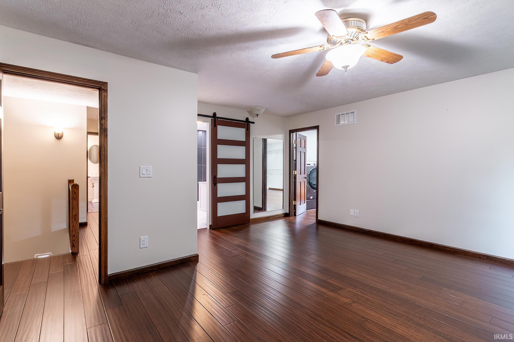 Empty bedroom with dark wood floors, a ceiling fan, and a frosted-glass barn door.