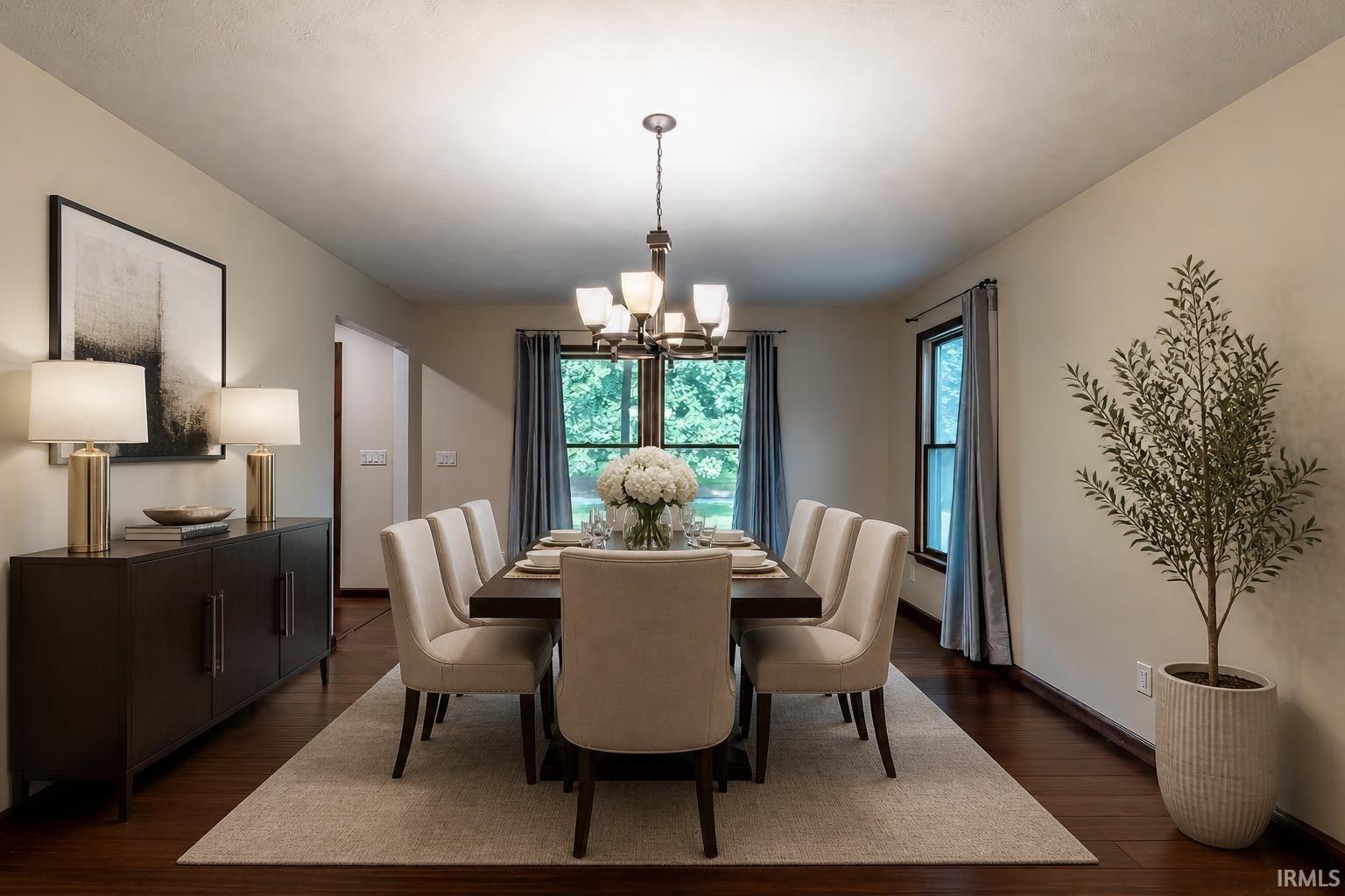 Dining room with a dark wood table, cream chairs, chandelier, and windows overlooking greenery.