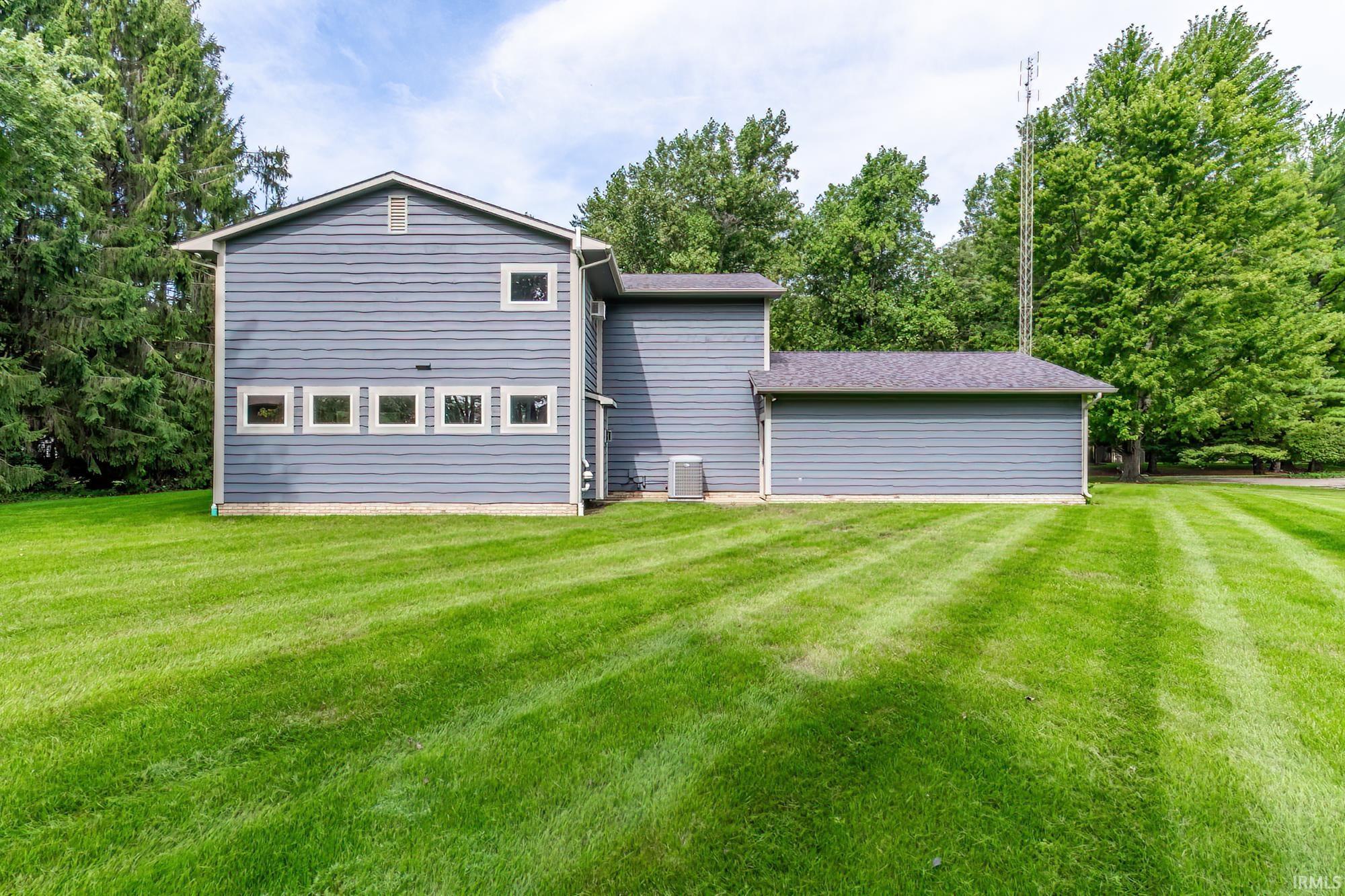 Gray-sided home with a broad mowed lawn, mature trees, and an antenna tower behind it.
