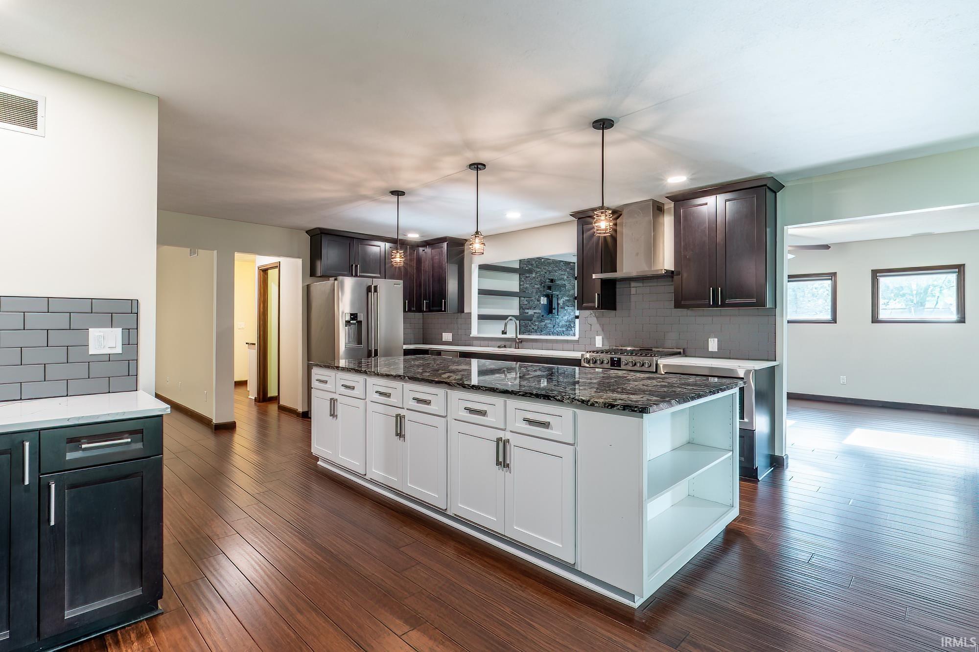 Modern kitchen with a large white island, dark cabinetry, stainless steel appliances, and adjoining room.