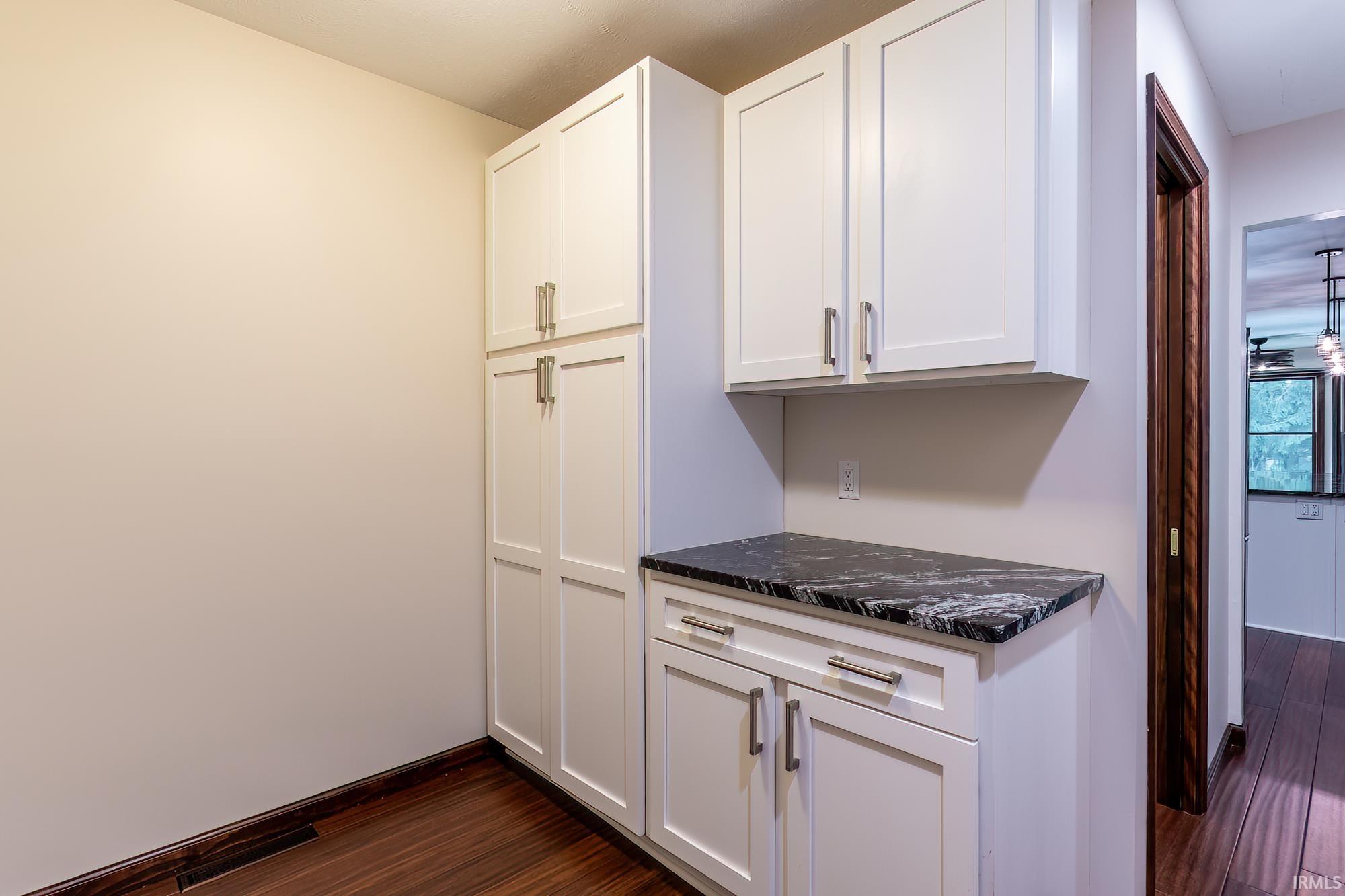 Kitchen with white shaker cabinets, a dark veined countertop, and dark hardwood floors.