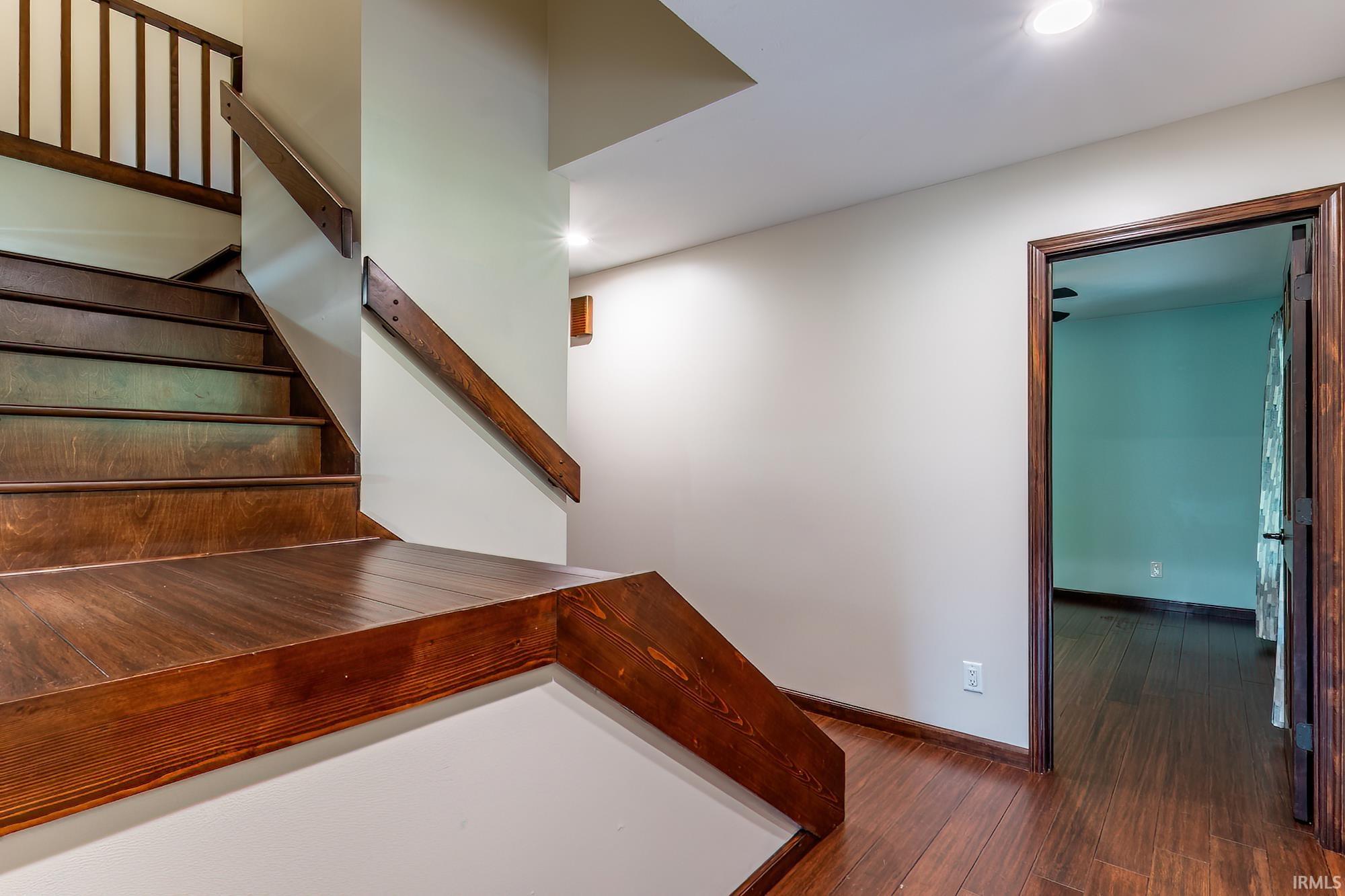 Wooden stair landing with dark railings and an open doorway to a teal room.