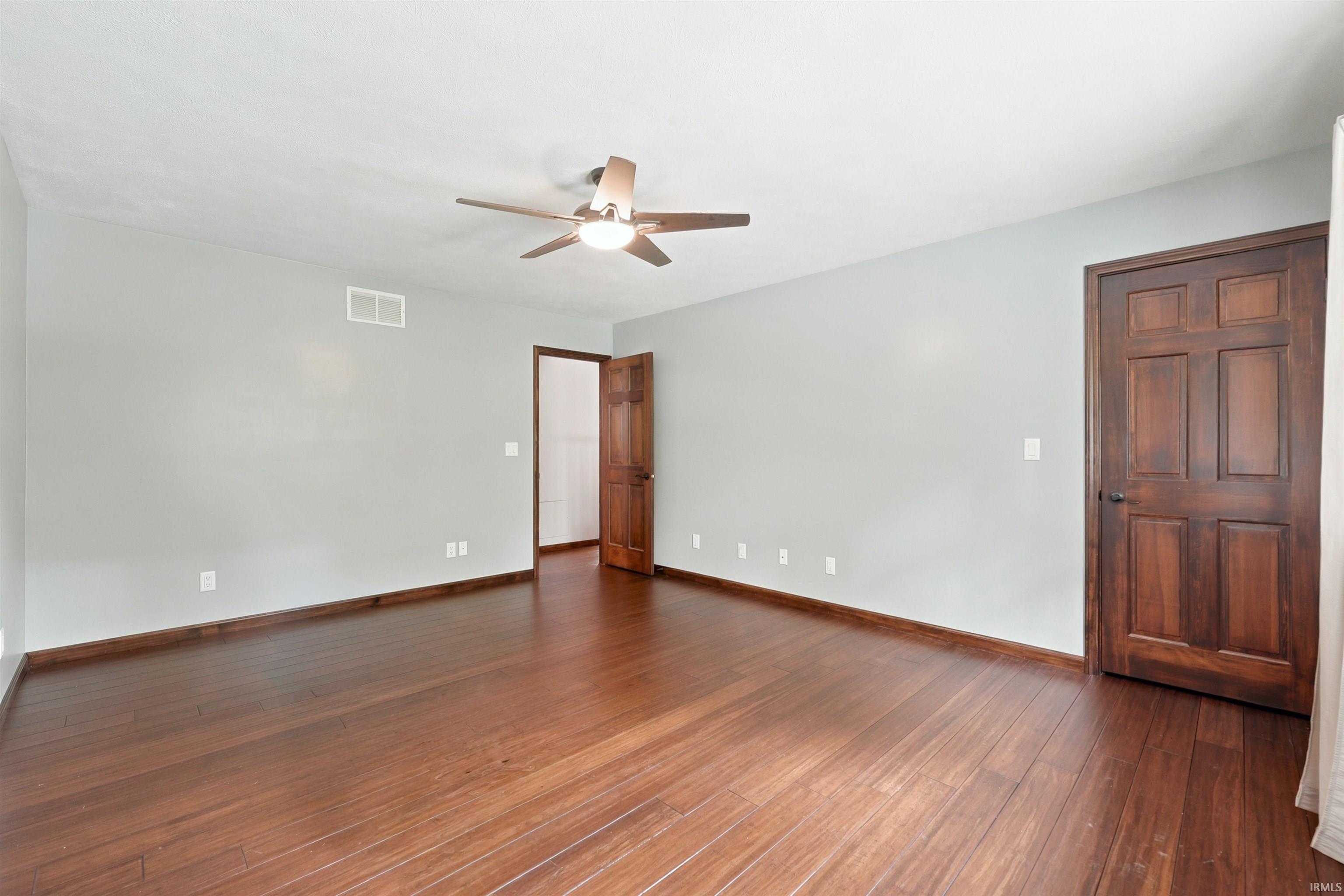 Empty room with reddish-brown wood floors, two dark wood doors, and a ceiling fan.