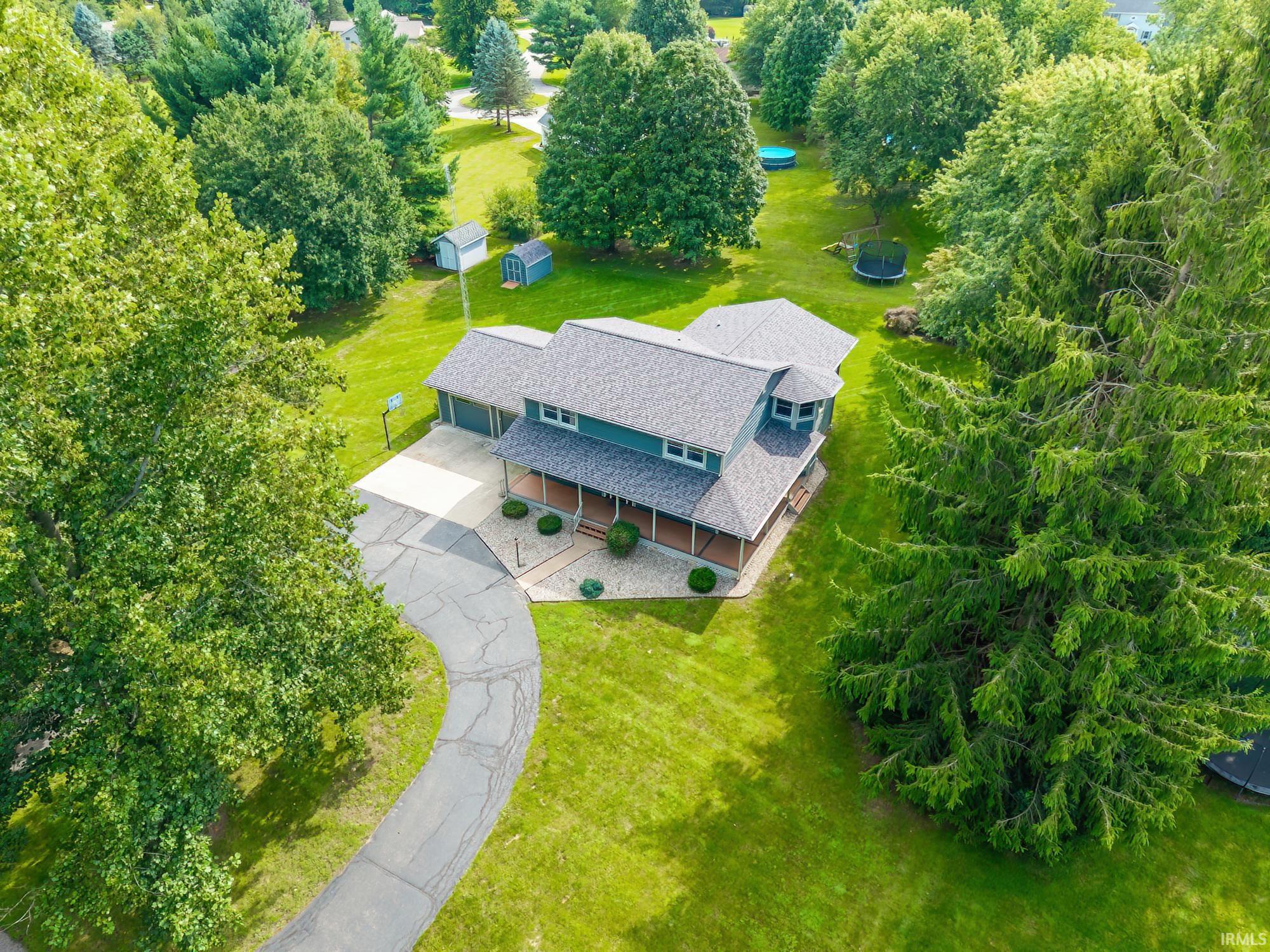 Aerial view of a two-story home with a curved driveway, covered porch, and spacious tree-lined yard.