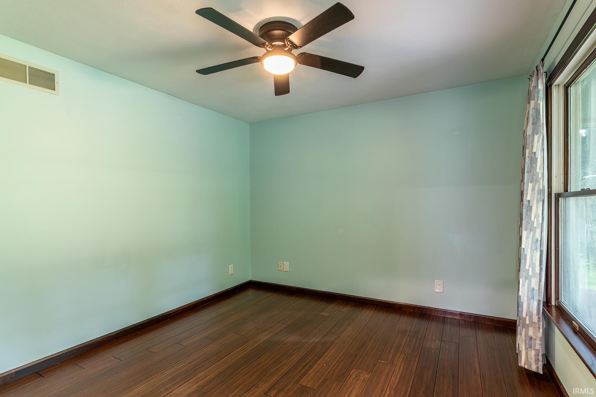 Empty room with dark wood flooring, pale blue-green walls, and a ceiling fan.