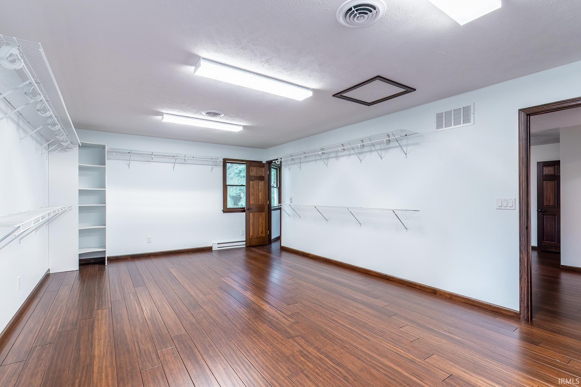 Empty walk-in closet with white wire shelving, built-in shelves, and dark wood-look flooring.