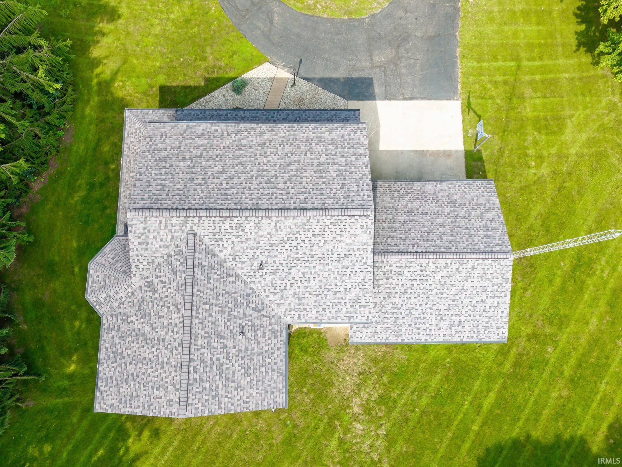 Aerial view of a house with a broad gray shingle roof, roof ladder, driveway, and green lawn.