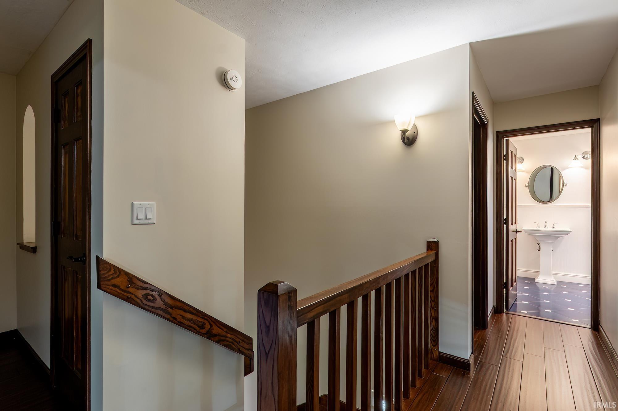 Hallway landing with a dark wood railing and an open doorway to a bathroom with a pedestal sink.